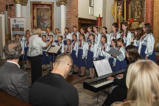 Na tle ołtarza stoi Chór Dziewczęcy Canzona - grupa młodsza, przed chórem dyrygentka Adrianna Wtorkowska- Kubińska
