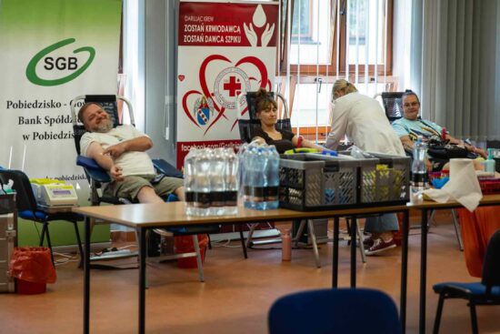 Sala w której postawione są trzy fotele, na których dwie kobiety i mężczyzna oddają krew
