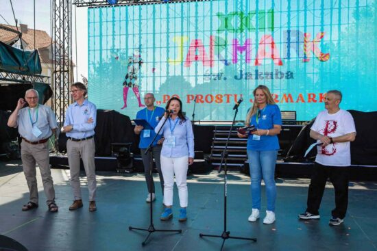Na scenie przy mikrofonie burmistrz Justyna Radomska, po lewej stronie stoją:zastępca burmistrza W ramach spektaku Street ShpowMarcin Buliński, ks. proboszcz Sławomir Jessa, za nimi dyrektor CKS Marcin Stroemich . Po prawej stronie Stanisław Woźniak