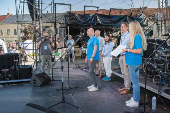 Na scenie przy mikrofonie stoi dyrektor CkiS Marcin Stroemich z tyłu stoją proboszcz Sławomir Jessa, burmistrz Justyna Radomska, zastępca burmistrza Marcin Buliński