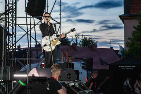 Nas scenie gwiazda wieczoru Dawid Kwiatkowski stojący przy mikrofonie z gitarą w ręku