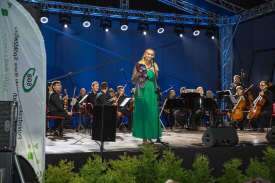 Na scenie kobieta w zielonej sukience za nią siedzi orkiestra