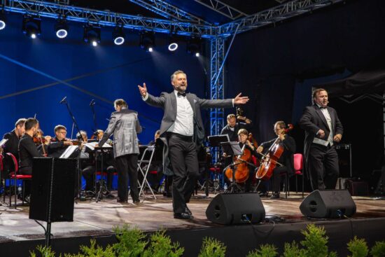 Na scenie stoi dwóch mężczyzn-za nimi orkiestra