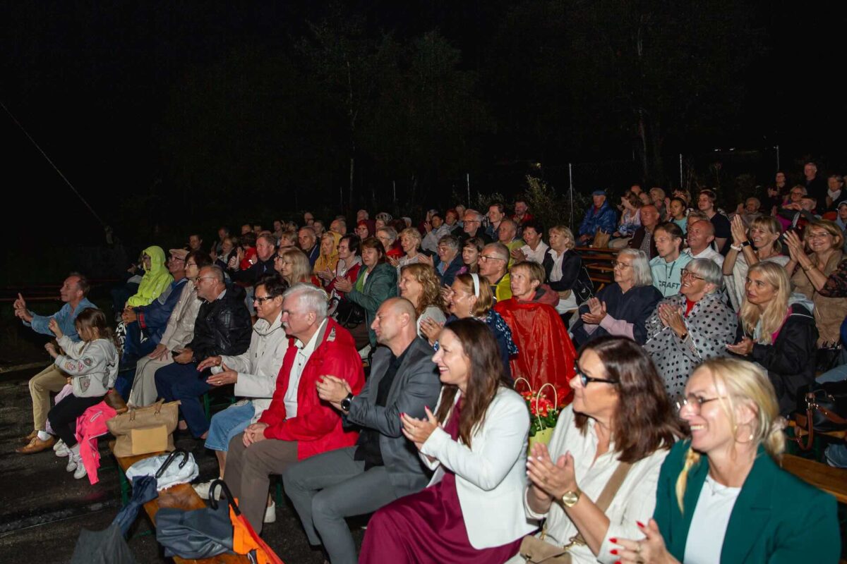 Siedząca na ławkach publiczność pod sceną 