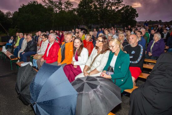 Siedząca na ławkach publiczność pod sceną 6 Sołtys Magdalena Matoga stoi wśród publiczność i trzyma koszyk  z koszykiem podczas kwesty 