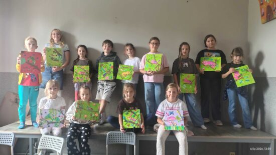 Grupa dzieci pozuje do zdjęcia ze sowimi pracami